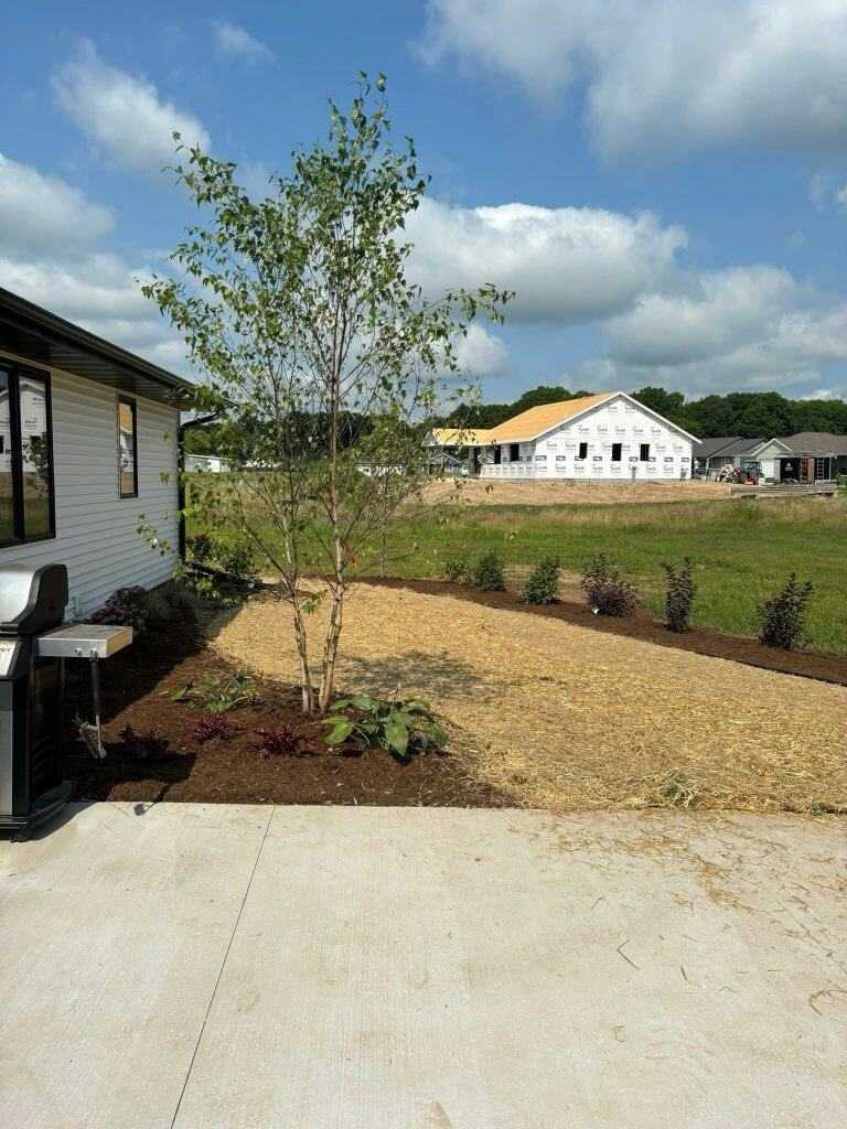 Layered front yard foundation planting with evergreens, shrubs, and perennials in a mulched bed on a Wisconsin home in Sheboygan County